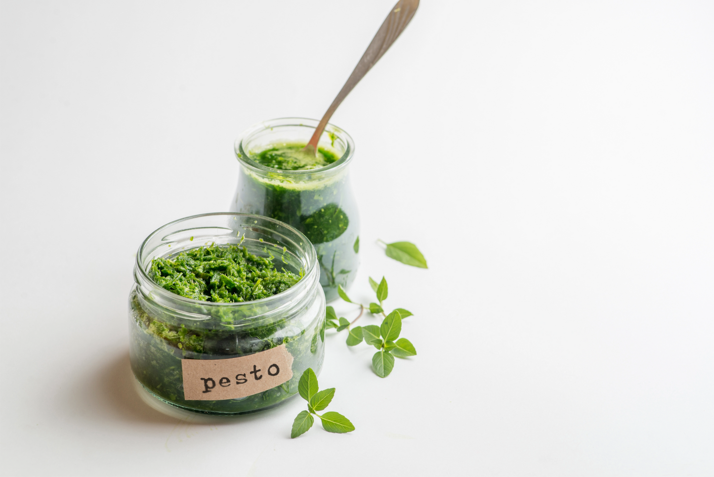 Two jars of pesto with a spoon on a light background