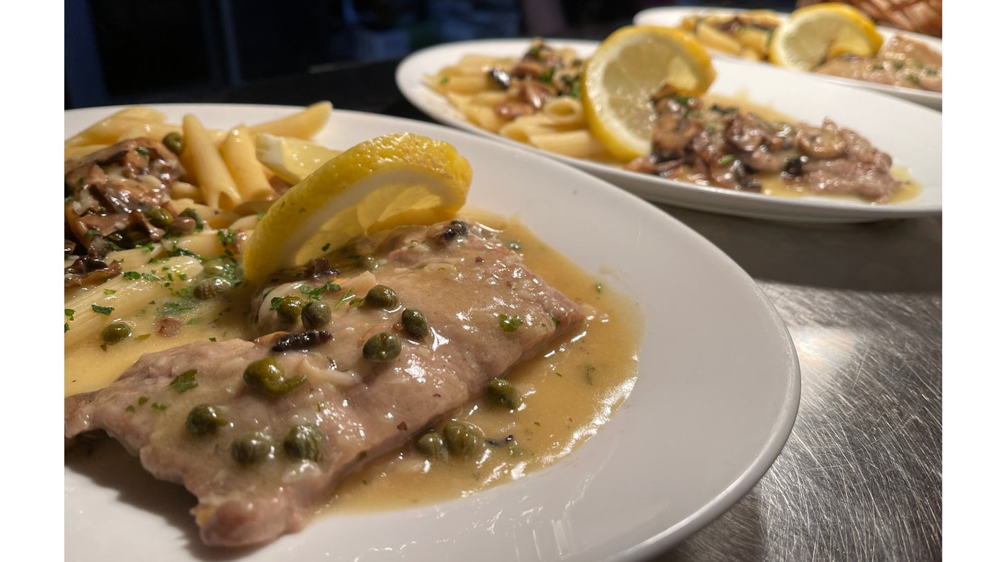 Plated dish of meat with sauce and lemon garnish on a table.