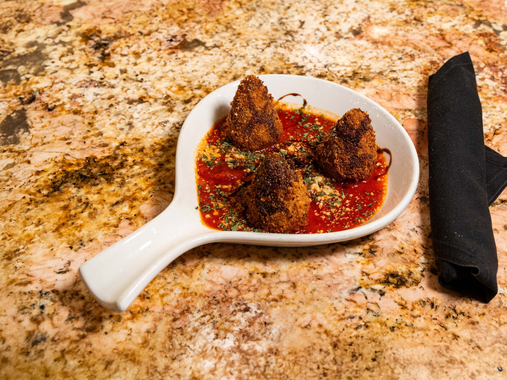White dish with fried items in red sauce on a textured stone surface