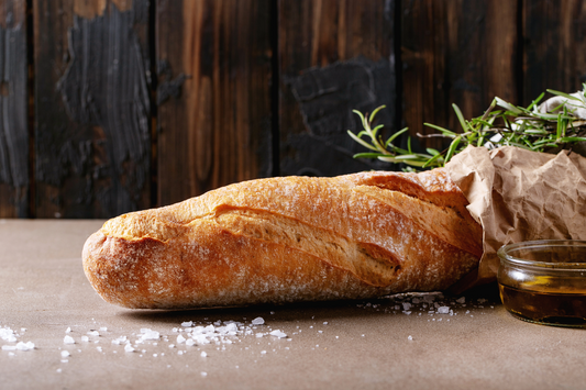 Loaf of bread on a wooden surface with rosemary and oil