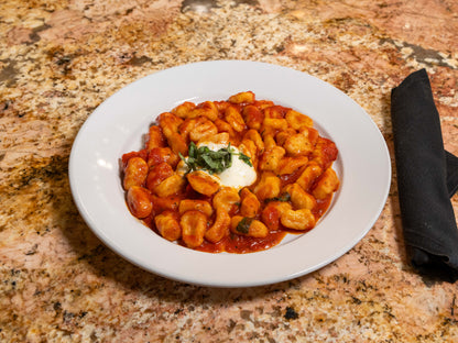 Plate of gnocchi with tomato sauce and a dollop of sour cream on a marble countertop.