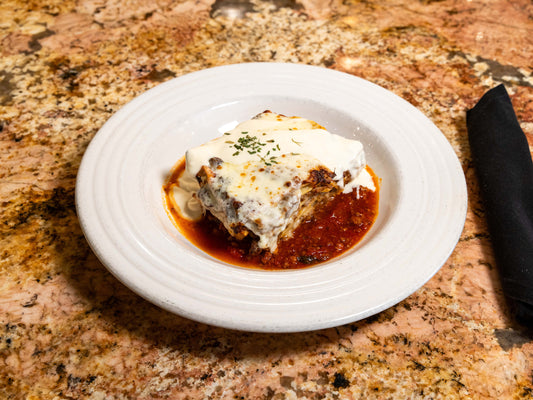 Lasagna on a white plate with tomato sauce on a marble countertop