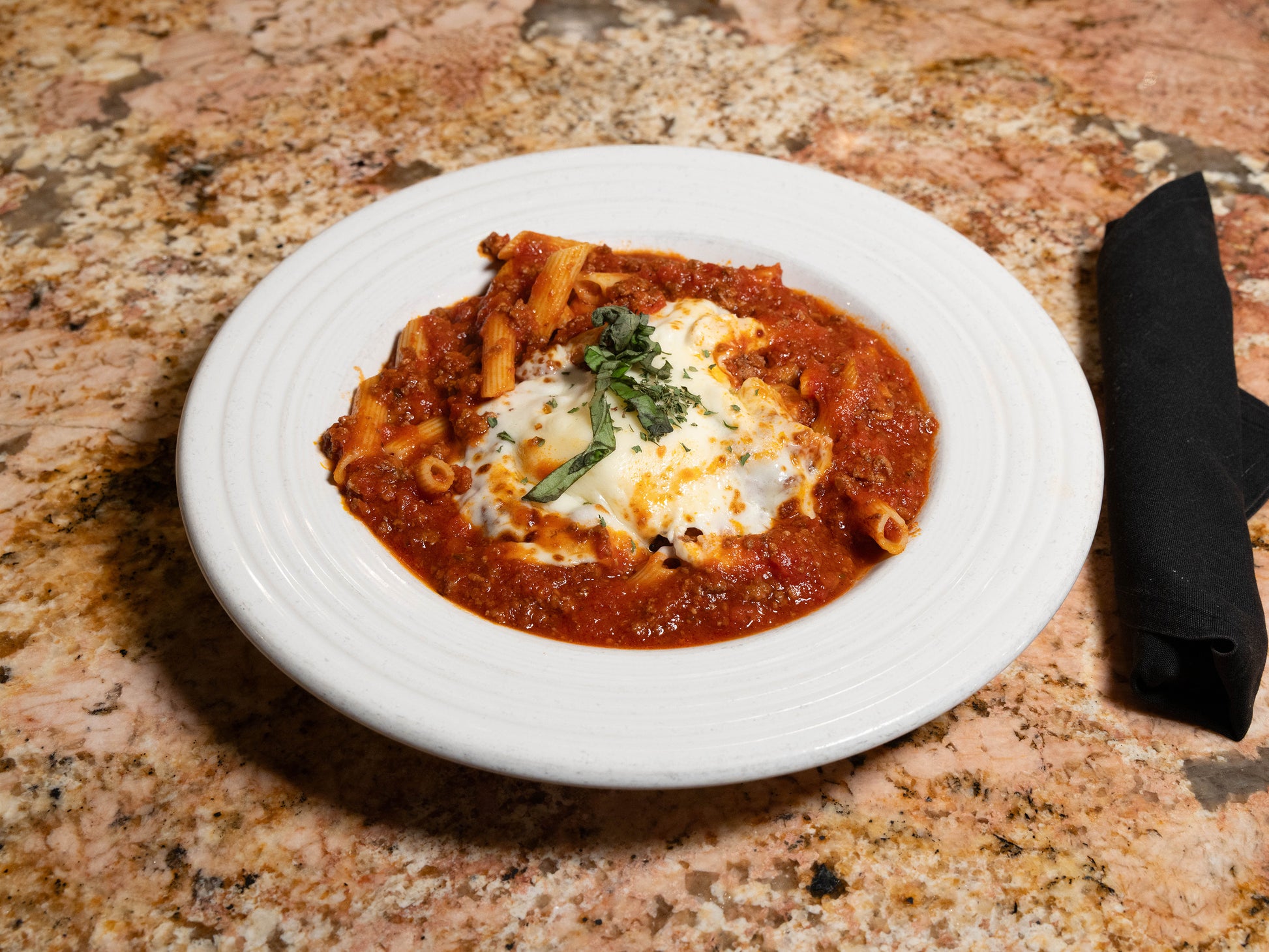 Pasta dish with tomato sauce and cheese on a white plate on a marble countertop